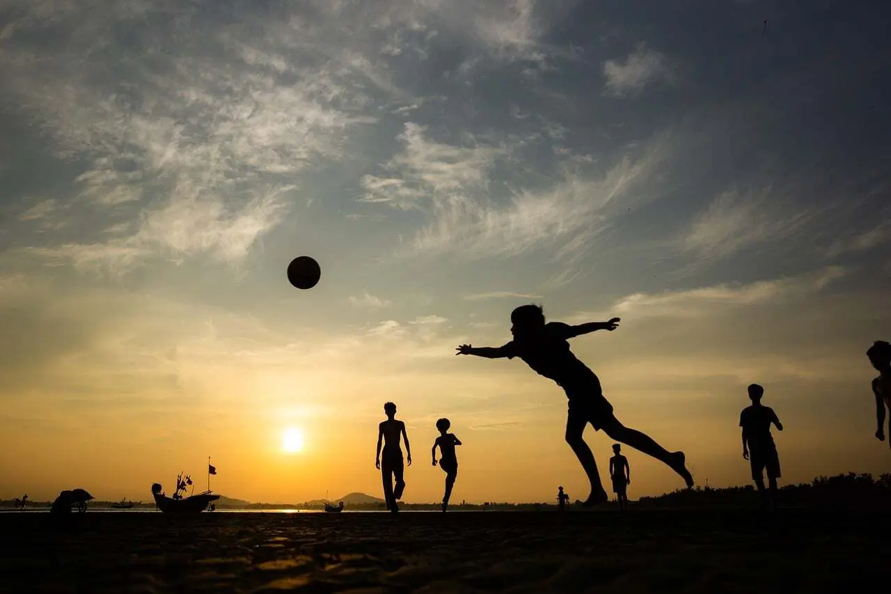 Siluetter av människor som spelar fotboll på stranden i solnedgången