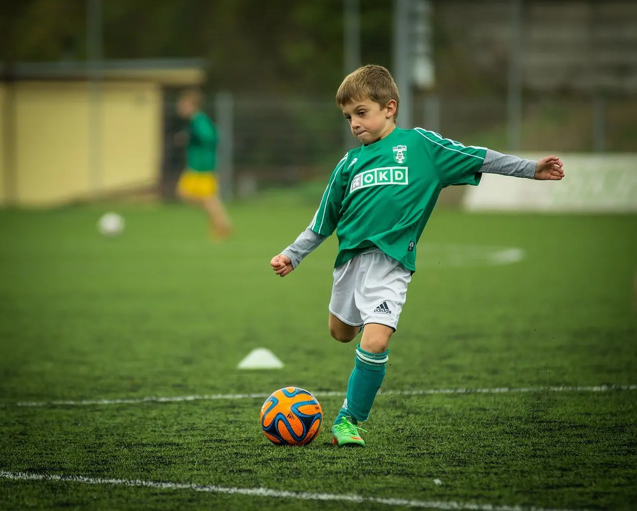 En pojke sparkar en boll på en fotbollsplan