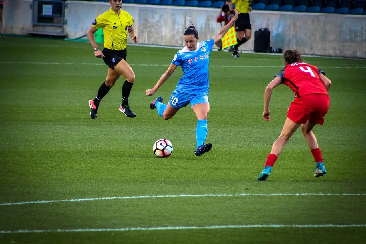 Kvinnlig fotbollsspelare i blå tröja skjuter under en match